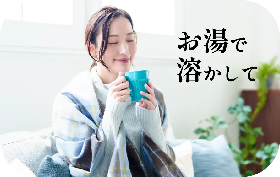 ブランケットにくるまり、マグカップを手にする女性