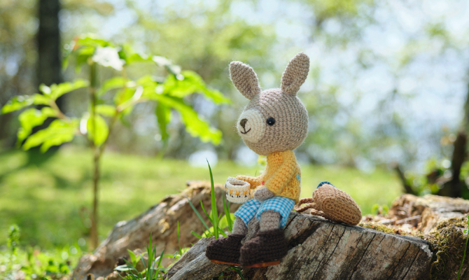 切り株に座る、ティーカップを持ったうさぎのあみぐるみ