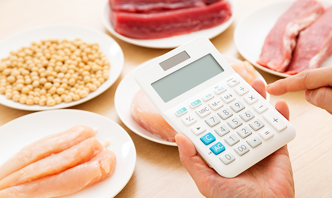 食材の前でタンパク質量を電卓で計算する手