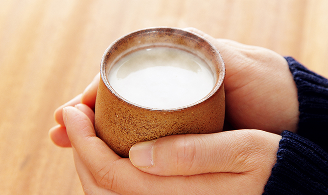甘酒が入った湯飲みを両手で持つ人