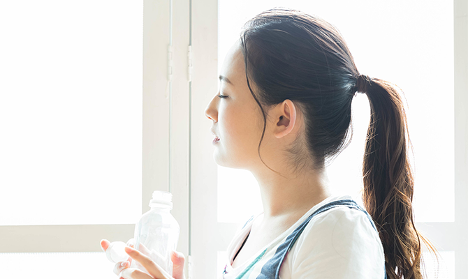 ペットボトルの水を飲み、目を閉じて休憩する女性。