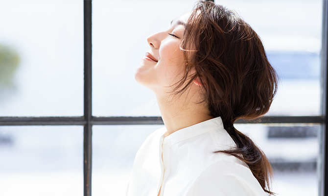 目を閉じて、顔を上に上げて深呼吸する女性