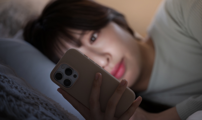夜にベッドの中でスマホを見る女性