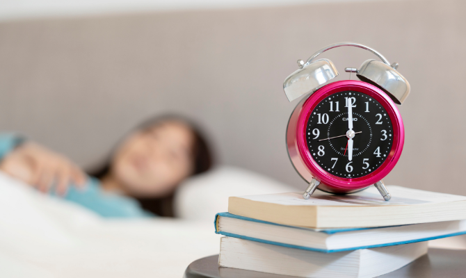 ベッドで寝ている女性と6時を指す目覚まし時計