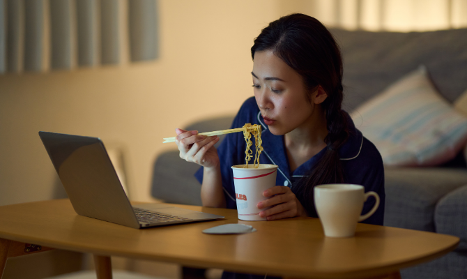 暗い部屋でカップラーメンを食べる女性