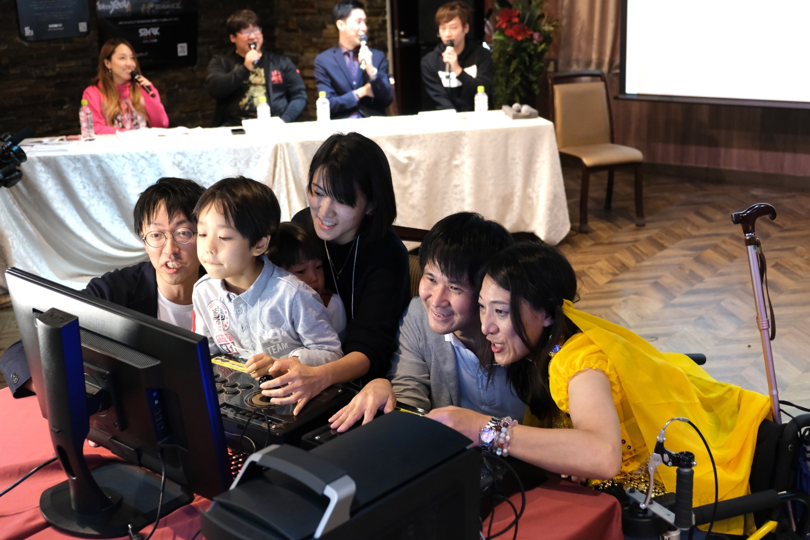 2019年11月に開催した最初のバリアフリーeスポーツの大会。加藤さんも家族で参加（左）し、パズルゲームで対戦。その様子をeスポーツのプロプレーヤーや車イス利用者が解説した（後ろ）。